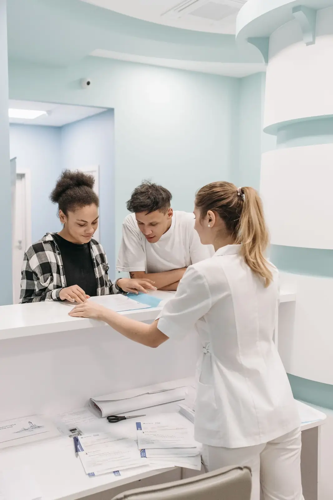 Recepção de uma clínica, com a recepcionista atendendo pacientes no balcão